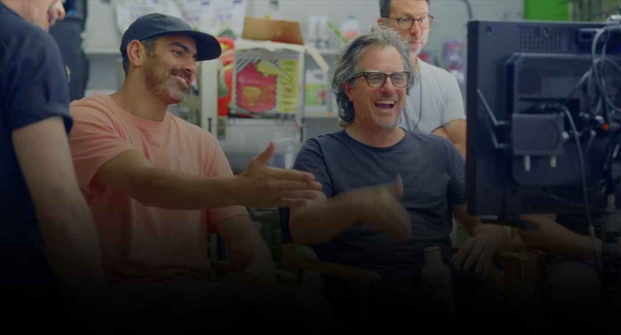 Gambar dua pembuat film laki-laki yang sedang duduk menonton dan memberi isyarat ke layar proyeksi.